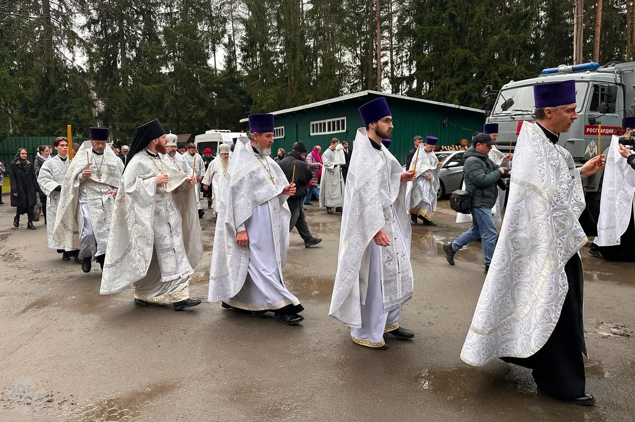 На церемонии в лесной зоне у Левашово чтят памяти погибших, звучат имена и возлагаются цветы под дождём; служба провела митрополит.